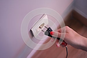 Closeup of woman holding in hand inserts plug into socket