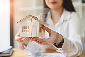 Closeup woman holding house model with flare light from window. Real estate, loan, mortgage and insurance concept