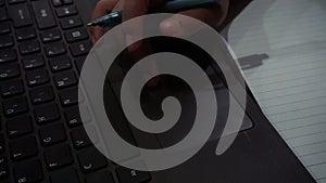 Closeup woman holding pen using touchpad and typing on black laptop keyboard. Doing online class, assignment, homework and study