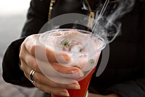 Closeup of woman holding plastic cup with vaporizing fruit tea