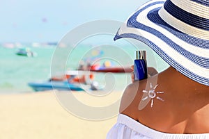 Closeup woman holding the sunblock bottle cream in hand, with sunblock lotion cream applied to her back and draw is the sun, at