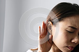 Closeup of Woman holds her hand near ear and listens carefully on grey background. Hearing problem  deaf concept