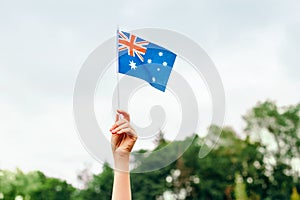 Closeup of woman human hand arm waving Australian flag against blue sky. Proud citizen man celebrating national Australia Day in