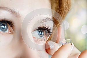 A closeup of a woman inserting a contact lens into her eye