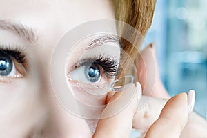 A closeup of a woman inserting a contact lens into her eye