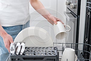 Closeup of woman loading dishwasher with cutlery and dishware