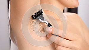 Closeup of woman with long armpit hair shaving and using razor in bath. Concept of hygiene, natural beauty, feminity and body hair