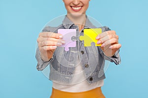 Closeup of woman in modern denim jacket smiling broadly and holding colorful pieces of puzzle, two parts of one
