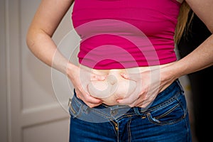 Closeup of woman pinching belly fat.