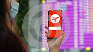 Closeup, woman, in protective mask, holds smartphone with airplane icon, pandemic sign, on screen, in front of flight