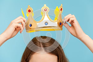 Closeup of woman putting on head golden crown, concept of awards ceremony, privileged status, superior position