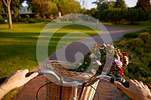 Closeup woman riding bicycle with flower basket handlebar view
