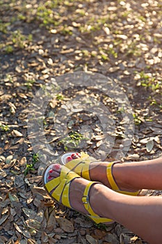 Closeup of woman`s feet in bright yellow sandals on the ground. Sunny summer day outdoors. woman walking in the park