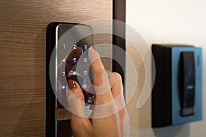 Closeup of a woman`s finger entering password code on the smart digital touch screen keypad entry door lock in front of the room