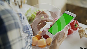 Closeup of woman`s hand browsing smartphone with green screen on kitchen at home