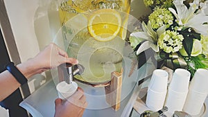 Closeup woman`s hand dispense water from a large glass jug with fresh sliced lemon inside in vintage tone.