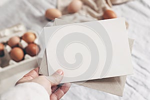 Closeup of woman`s hand holding blank paper card. Greeting card mock-up scene. Spring, Easter design. Feminine styled