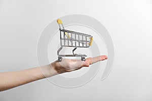 Closeup of a woman`s hand holding a small metal empty shopping cart in the palm of her hand on gray background. The concept of