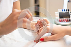 Closeup of a woman's hand in a nail salon receiving a manicure by a beautician with nail file