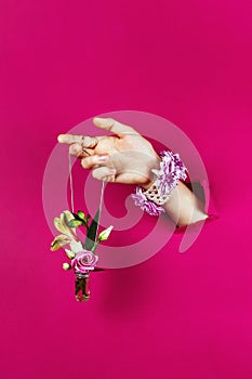 Closeup of woman`s hand through torn paper holding bottle with bouquet on a silver chain