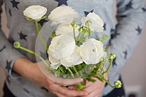 Closeup of woman's hands golding a bunch of beautiful white ranunculus. Grild with bouquet of flowers. Ranunculus