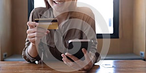 Closeup woman's hands holding a credit card and using smartphone for online shopping.