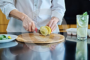 Closeup of a woman's hands preparing cold cocktail with lemon, mint leaves and ice