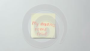 Closeup woman`s hands stick yellow sticker paper sheets with words my dreams come true.