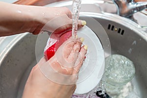 Close up woman`s hands of washing dishes in kitchen sink. Cleaning chores