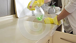 Closeup on woman`s hands in yellow protective gloves cleaning kitchen furniture