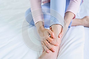 Closeup woman sitting on bed holds her ankle injury, feeling pain. Health care and medical concept