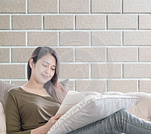 Closeup woman sitting on sofa for reading a book in free time in the afternoon on brick wall textured background , relax time of a