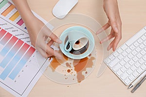 Closeup of woman spilled coffee on office desk, top view