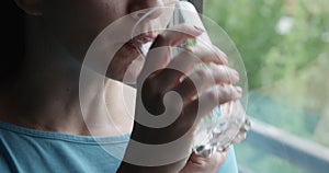 Closeup of Woman Taking a Pill and Drinking Water by the Window
