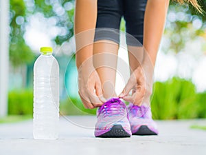 Closeup of woman tying shoe laces. Female sport fitness runner getting ready for jogging with water bottle