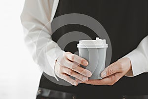 closeup woman wearing apron holding paper cup of hot coffee