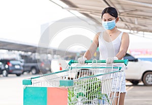 Closeup woman wearing face mask for protect air polution or virus covid 19 with shopping cart in supper market, selective focus