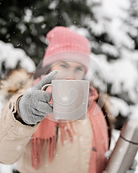 Closeup of woman in winter clothes holding a mug with hot tea or coffee outdoors in snowy day