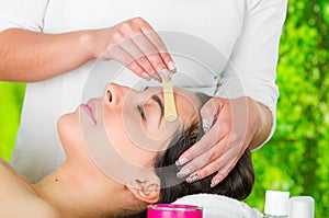 Closeup womans face receiving facial hair waxing treatment, hand using wooden stick to apply wax, beauty and fashion