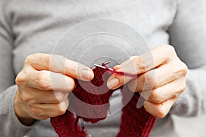 Closeup womans hands knits red burgundy wool yarn with knitting needles.