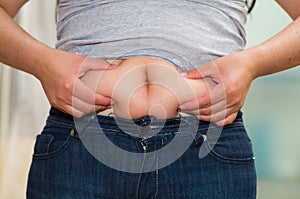 Closeup womans stomach wearing jeans, grabbing onto excessive fat using fingers, belly button revealed, weightloss photo
