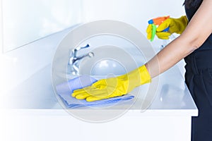 Closeup women hand maid or charwoman cleaning modern new basin in bathroom. Water tap clean using yellow gloves and blue cloth photo