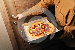 Closeup women hands hold a box of new pizza. The girl opens the door and holds pepperoni