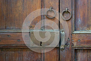 Closeup of a wooden aged latch and two rusted ring door knockers over an ornate wooden door