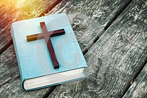 Closeup of wooden Christian cross on bible, burning candle and prayer beads on the old table.