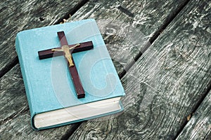 Closeup of wooden Christian cross on bible, burning candle and prayer beads on the old table.