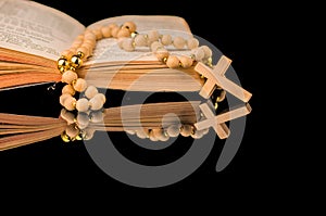 Closeup of wooden Christian cross on bible and prayer beads on black.Church utensils