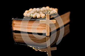 Closeup of wooden Christian cross on bible and prayer beads on black.Church utensils