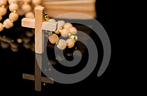 Closeup of wooden Christian cross on bible and prayer beads on black.Church utensils