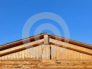 Closeup of wooden facade and roof under blue sky. New rural wooden house fragment with roof. Wooden beam structure. Architecture